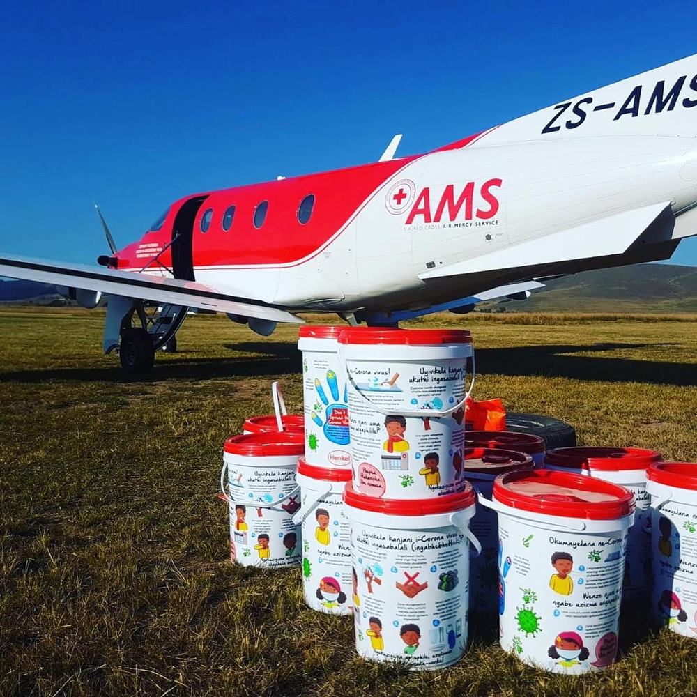 Hygiene kits printed in isiZulu stacked beside a Pilatus PC-12 on a grass airstrip during pandemic relief flights