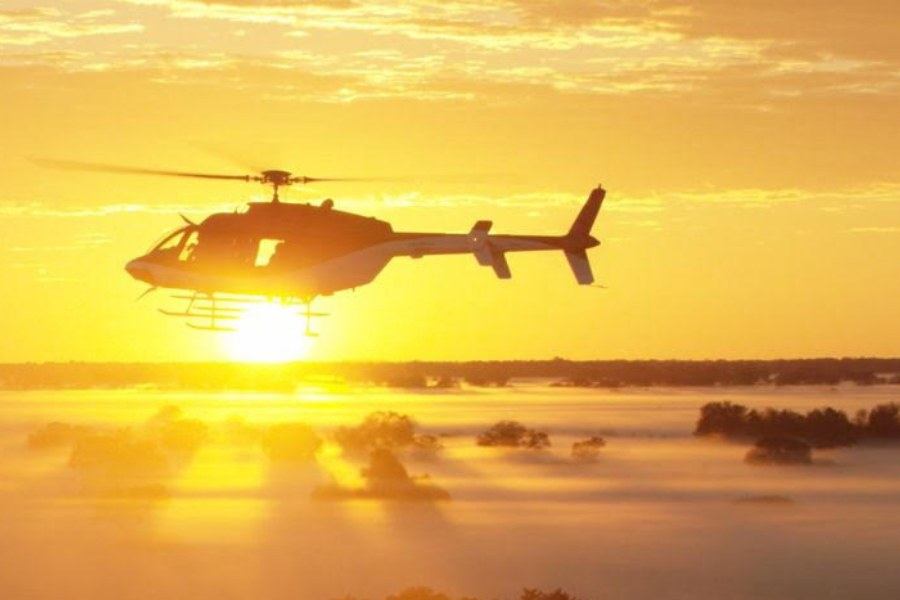 Helicopter silhouetted against sunrise mist over the African bush at the start of a first-light sortie
