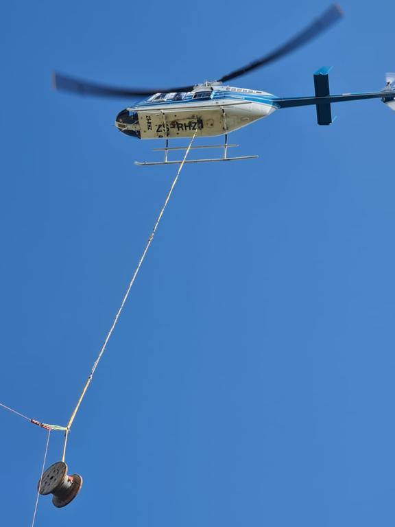 Bell 206 LongRanger helicopter lifting a cable drum on a longline during transmission tower construction