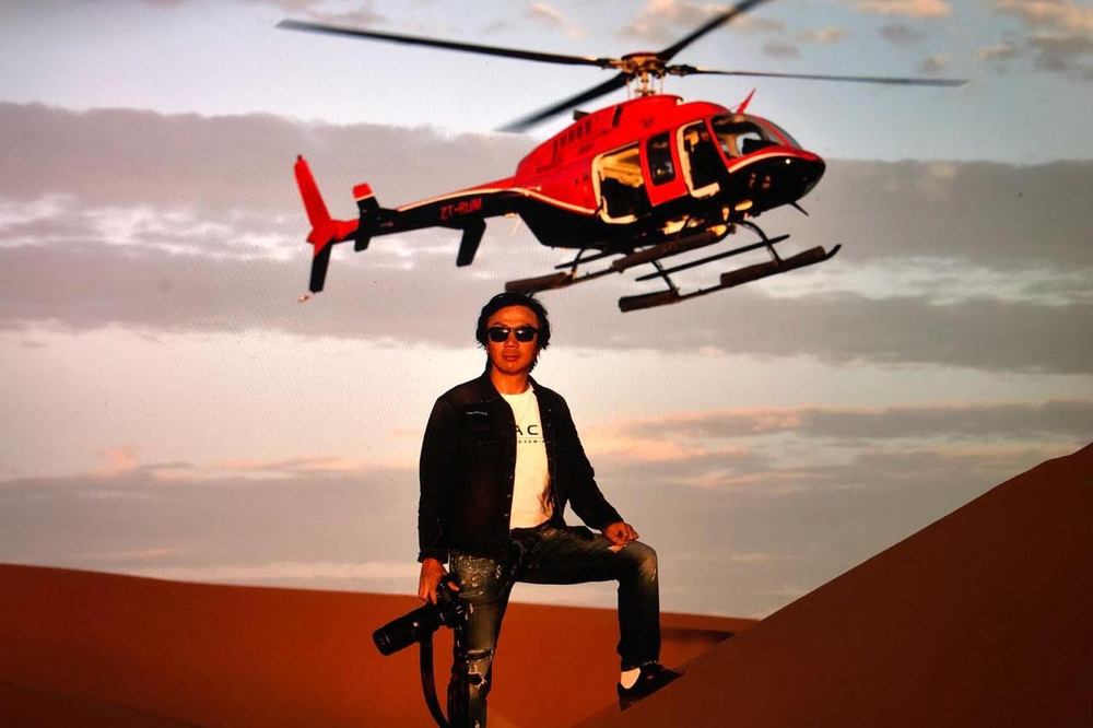 Bell 407 helicopter hovering above a Namib desert dune during a photographic expedition charter