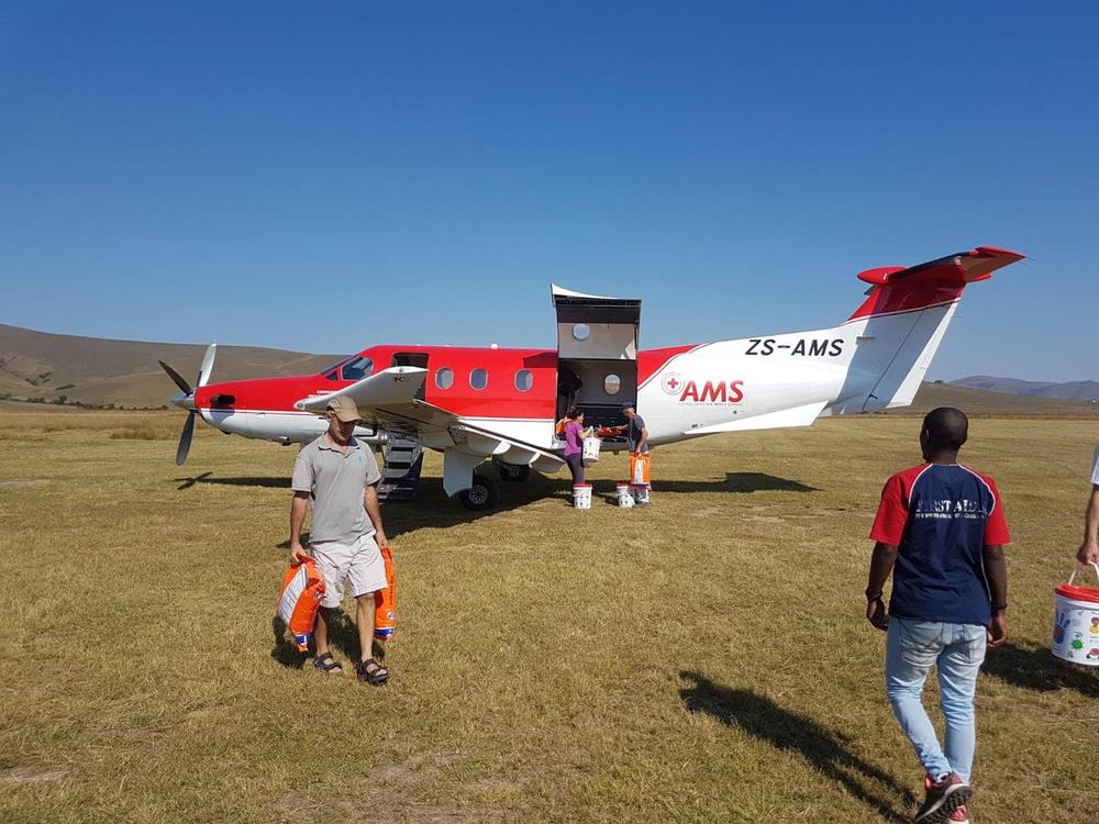 Pilatus PC-12 in air mercy service livery unloading relief supplies by hand on a rural grass airstrip