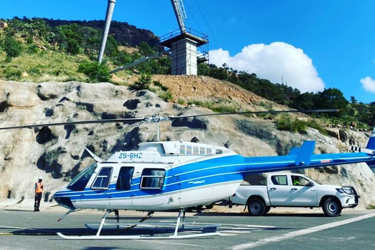 Helicopter at a hillside transmission tower site before underslung cable lifting