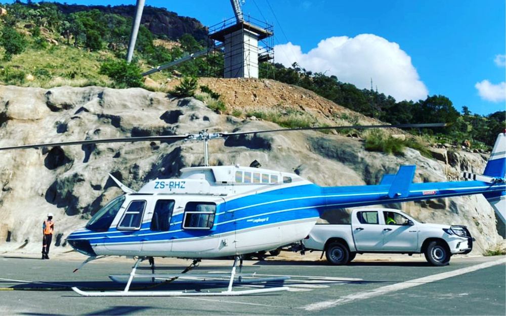 Bell 206 LongRanger ZS-RHZ at a hillside transmission tower construction site before underslung lifting work