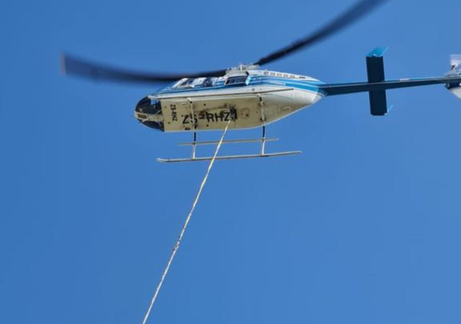A cable drum suspended on a longline beneath a helicopter, being placed onto a tower footing on a remote ridge