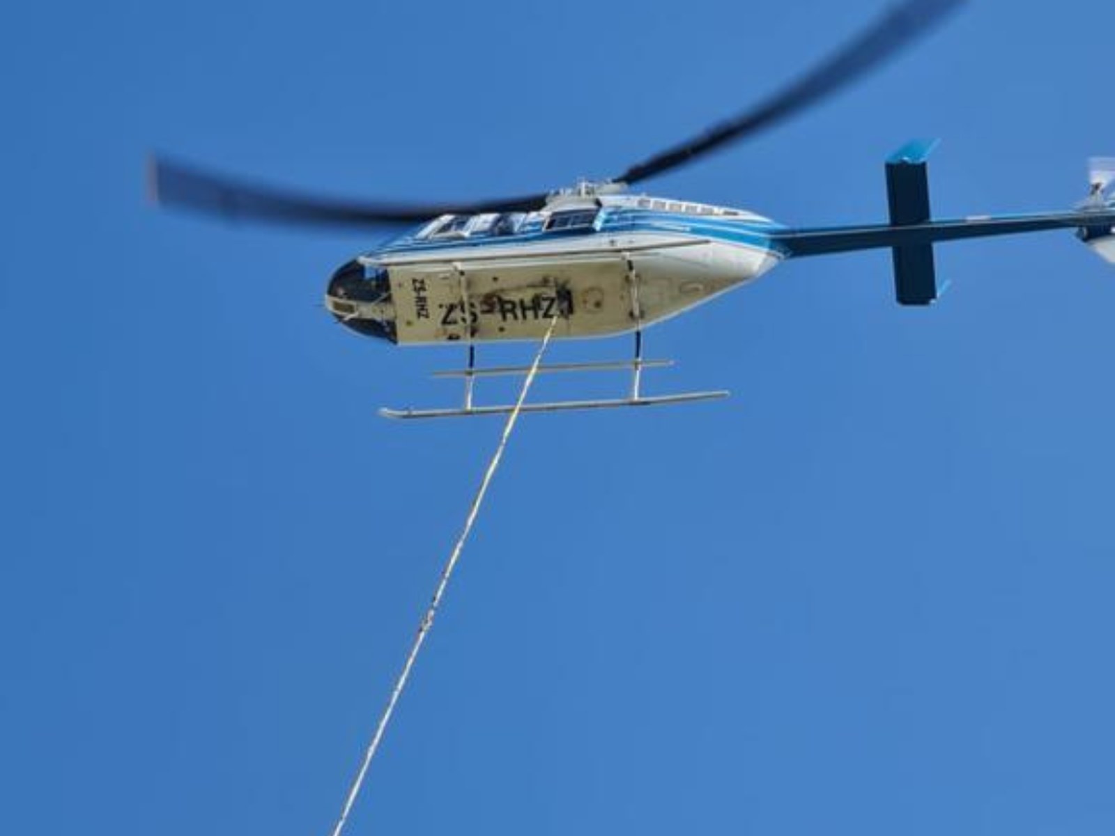 A cable drum suspended on a longline beneath a helicopter, being placed onto a tower footing on a remote ridge