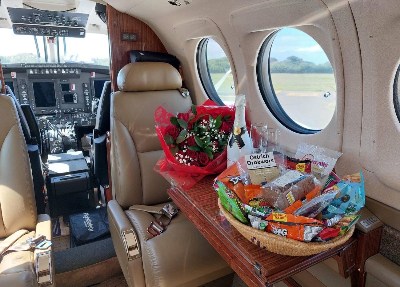 King Air cabin table set with red roses, chilled champagne and South African snacks including ostrich droëwors