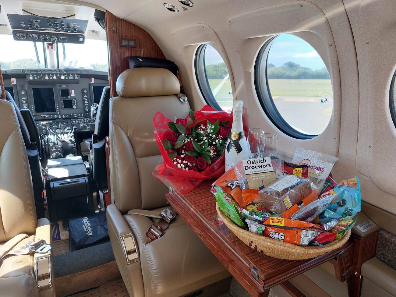 King Air cabin table set with red roses, chilled champagne and South African snacks including ostrich droëwors